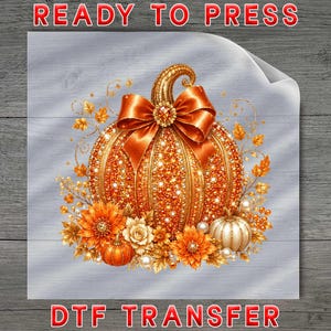 May include: A DTF transfer sheet featuring a large, orange, jewel-encrusted pumpkin adorned with a prominent orange satin bow at the top. The design includes smaller pumpkins, orange flowers, golden leaves, and white pearls. Text reads READY TO PRESS DTF TRANSFER.