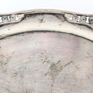 Puede incluir: Primer plano de un plato de plata deslustrado con un borde ornamental y decorativo. El plato tiene una forma ligeramente octogonal con una superficie lisa y reflectante. El borde presenta un patr&oacute;n repetitivo de peque&ntilde;os c&iacute;rculos.