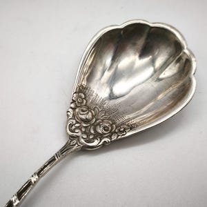 Peut inclure: Une cuill&egrave;re de service en argent avec un bol festonn&eacute; et un motif floral sur le manche. La cuill&egrave;re pr&eacute;sente un motif d&eacute;taill&eacute; et un manche d&eacute;coratif. La cuill&egrave;re est en m&eacute;tal brillant et r&eacute;fl&eacute;chissant.