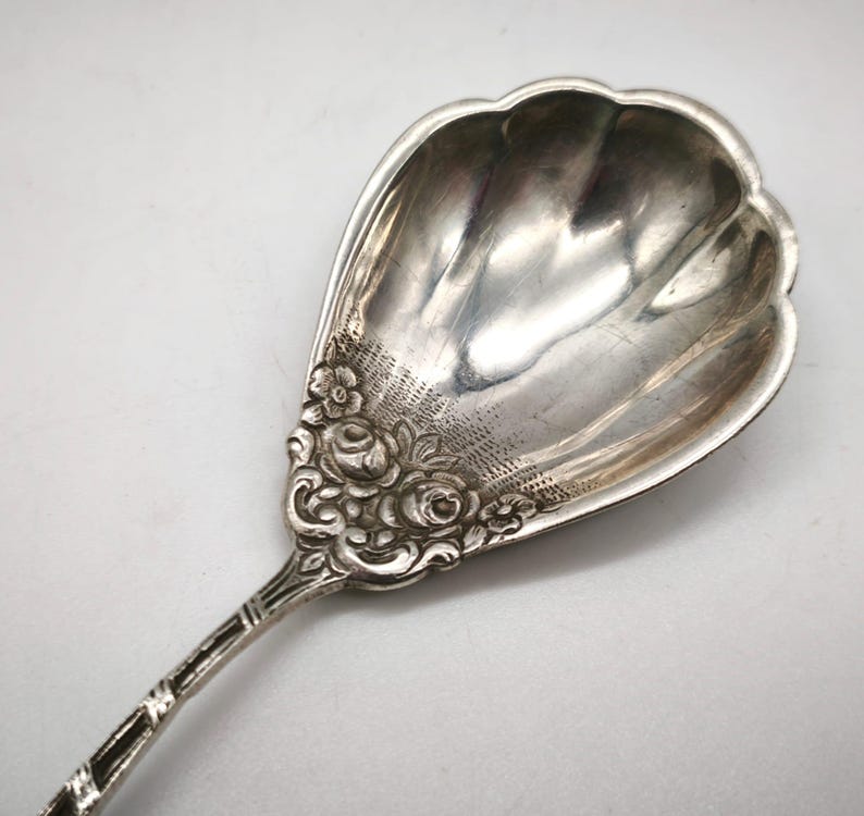 Peut inclure: Une cuill&egrave;re de service en argent avec un bol festonn&eacute; et un motif floral sur le manche. La cuill&egrave;re pr&eacute;sente un motif d&eacute;taill&eacute; et un manche d&eacute;coratif. La cuill&egrave;re est en m&eacute;tal brillant et r&eacute;fl&eacute;chissant.