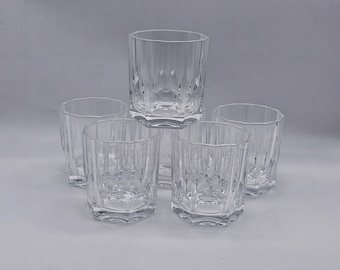 May include: A collection of five clear, patterned drinking glasses. The glasses feature a geometric design with vertical lines and a hexagonal base. The glasses are arranged in a pyramid shape, with one glass on top and four below.