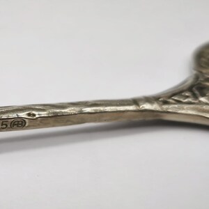 May include: Close-up of a silver serving utensil with an ornate, floral design. The handle has a textured surface and the hallmark "835" is visible. The utensil is likely vintage and used for serving food.