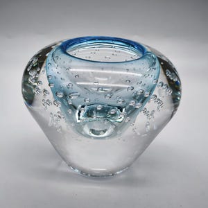 May include: A clear glass vase with a blue rim and air bubbles throughout. The vase has a rounded, organic shape.