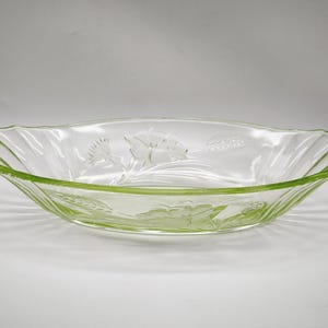 Op de afbeelding: Heldere glazen serveerschaal met een lichtgroene rand en bloemenmotief. De ovaalvormige schaal heeft reliëfbloemen en tarwearen. De randen hebben een geschulpte vormgeving. Een vintage stuk om eten te serveren.