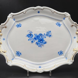 May include: A white porcelain serving tray with gold trim and blue floral designs. The tray has two handles and is oval shaped.