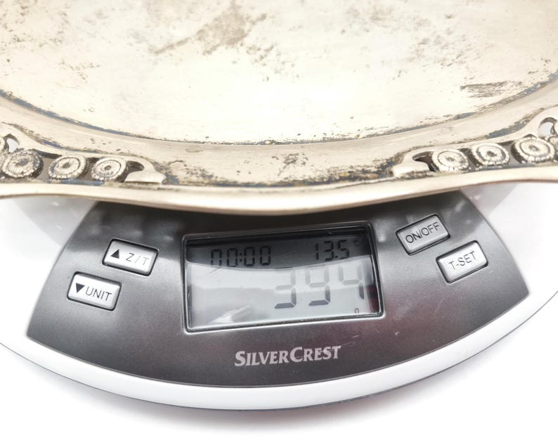 Puede incluir: Una bandeja plateada ornamentada se coloca sobre una b&aacute;scula de cocina digital. La b&aacute;scula muestra un peso de 394 gramos y una temperatura de 13,5 grados Celsius. La b&aacute;scula es de la marca SilverCrest.
