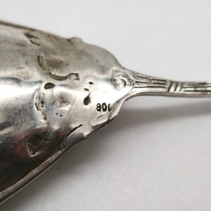 Peut inclure: Gros plan sur une cuill&egrave;re en argent au design orn&eacute;. La cuill&egrave;re a une surface textur&eacute;e et le chiffre "800" est estampill&eacute; sur le manche. La cuill&egrave;re est probablement antique ou vintage.