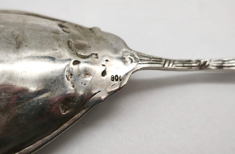Peut inclure: Gros plan sur une cuill&egrave;re en argent au design orn&eacute;. La cuill&egrave;re a une surface textur&eacute;e et le chiffre "800" est estampill&eacute; sur le manche. La cuill&egrave;re est probablement antique ou vintage.