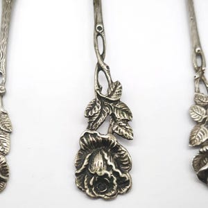 May include: Three antique silver spoons with intricate floral rose and leaf designs. The spoons have detailed stems and rose-shaped bowls, showcasing a vintage aesthetic.