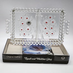 May include: A clear glass divided serving tray with a beaded edge and a floral design. The tray has two sections and is in its original box. The box is black with white text that reads "Original Walther Glas" and "Spaß mit Walther Glas".