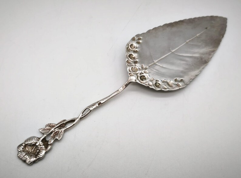 Peut inclure: Une pelle &agrave; g&acirc;teau argent&eacute;e avec une lame en forme de feuille et un motif floral sur le bord. La poign&eacute;e torsad&eacute;e se termine par une fleur, cr&eacute;ant une esth&eacute;tique &eacute;l&eacute;gante et vintage.