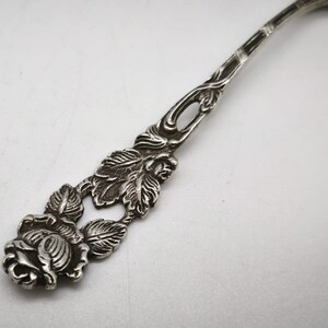 Peut inclure: Gros plan d'une cuill&egrave;re en argent avec un motif de rose. Le manche de la cuill&egrave;re pr&eacute;sente un motif complexe de feuilles et une rose d&eacute;taill&eacute;e &agrave; la base. La cuill&egrave;re est en m&eacute;tal brillant.