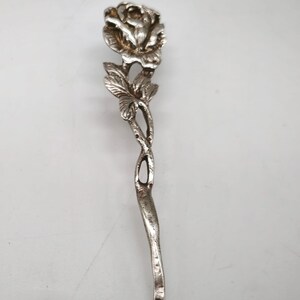 Peut inclure: Une cuill&egrave;re de service argent&eacute;e avec un motif de rose. La cuill&egrave;re pr&eacute;sente une fleur de rose d&eacute;taill&eacute;e en haut, avec des feuilles et une tige incurv&eacute;e. La poign&eacute;e a un design torsad&eacute; d&eacute;coratif.