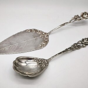 Peut inclure: Ensemble de service argent&eacute; comprenant une pelle &agrave; g&acirc;teau en forme de feuille et une cuill&egrave;re. Les deux pi&egrave;ces pr&eacute;sentent des d&eacute;tails floraux orn&eacute;s sur les manches et les bords. La pelle a une grande feuille.
