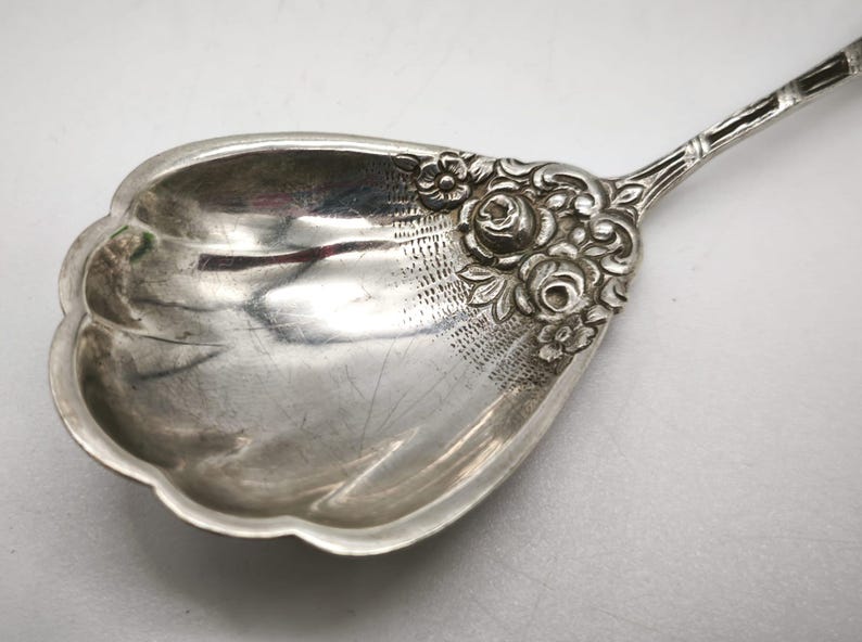 Peut inclure: Une cuill&egrave;re de service en argent avec un motif floral d&eacute;coratif. Le bol de la cuill&egrave;re a un bord festonn&eacute; et est orn&eacute; de d&eacute;tails grav&eacute;s. La poign&eacute;e pr&eacute;sente un motif floral d&eacute;taill&eacute;, ajoutant &agrave; son aspect &eacute;l&eacute;gant. La cuill&egrave;re est probablement vintage.