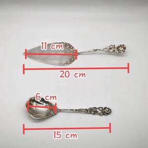 Peut inclure: Deux ustensiles de service argent&eacute;s. Le serveur &agrave; tarte mesure 20 cm de long et 11 cm de large. La cuill&egrave;re mesure 15 cm de long et 6 cm de large. Les deux ont des motifs de roses florales sur les manches.
