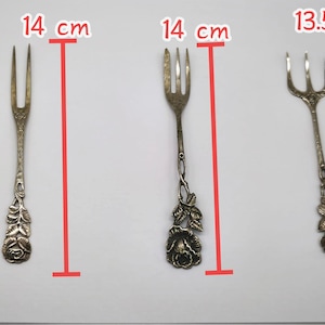 May include: Three antique silver forks, each approximately 5.5 inches long, are displayed against a white background. The forks have decorative floral designs on the handles. The tines vary in number, with two or three tines per fork.