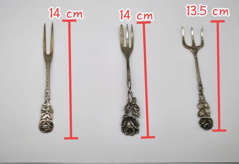 May include: Three antique silver forks, each approximately 5.5 inches long, are displayed against a white background. The forks have decorative floral designs on the handles. The tines vary in number, with two or three tines per fork.