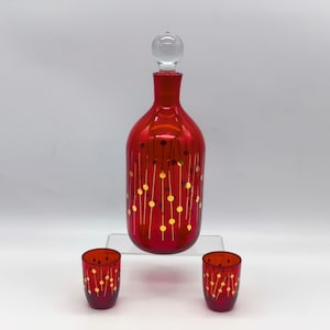 Puede incluir: Una jarra de cristal roja con un tapón de cristal transparente y dos vasos de chupito a juego. El conjunto está decorado con puntos y líneas doradas. La jarra mide aproximadamente 25 cm de altura.