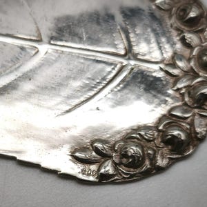 Peut inclure: Gros plan d'une pi&egrave;ce de service en argent en forme de feuille, avec des nervures d&eacute;taill&eacute;es. Le bord est orn&eacute; de roses en relief. La pi&egrave;ce a une surface brillante et r&eacute;fl&eacute;chissante et semble &ecirc;tre antique ou vintage. Le chiffre "800" est estampill&eacute; sur la feuille.