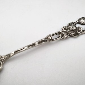 Peut inclure: Une cuill&egrave;re en argent avec un motif de rose sur le manche et le bol. La poign&eacute;e pr&eacute;sente des sculptures d&eacute;taill&eacute;es de roses et de feuilles, ajoutant une touche d&eacute;corative. La cuill&egrave;re est probablement en argent sterling ou en m&eacute;tal similaire.