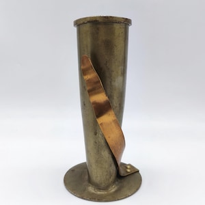 May include: An antique brass vase with a cylindrical body and a flared base. A copper-coloured metal strip wraps around the vase. The vase has a tarnished, aged appearance, suggesting it is an antique. The vase is designed to hold flowers.