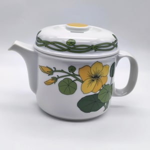 Peut inclure: Théière en céramique blanche avec un motif de fleurs jaunes et de feuilles vertes. La théière a un couvercle avec un bouton jaune et un motif de vigne verte.