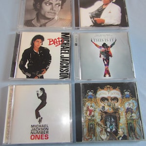 May include: Six Michael Jackson CD albums in clear plastic cases. The album covers feature images of Michael Jackson in various poses and outfits. Titles include "The Essential Michael Jackson", "Bad", and "This Is It".