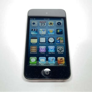 May include: A black Apple iPod Touch digital media player with a glass touchscreen display. The screen shows a grid of colorful application icons including FaceTime, Calendar, Photos, Camera, Videos, Maps, Weather, Passbook, Notes, Reminders, Clock, Game Center, Newsstand, iTunes, App Store, Settings, Messages, Mail, Safari, and Music.