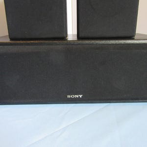 May include: A black Sony speaker system with a rectangular center speaker and two smaller speakers stacked on top. The speakers have a mesh front and the Sony logo is visible.