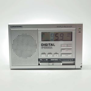 May include: A silver Grundig G1000A digital world receiver radio featuring a speaker grille on the left, a digital display showing 95.9 MHz, and various control buttons labelled Hour, Minute, Light, Alarm, and Sleep. The front panel includes text.