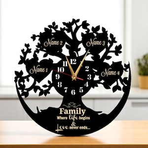 Könnte beinhalten: Schwarze Familienbaum-Uhr mit goldenen Zeigern. Die Uhr zeigt die Worte "Family Where life begins & Love never ends..." und Platz für vier Namen. Die Uhr steht auf einer Holzoberfläche.