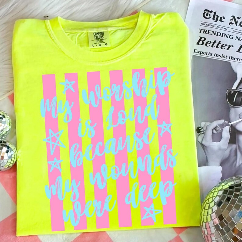 May include: A neon yellow t-shirt with the text "My worship is loud because my wounds were deep" in light blue script and pink vertical stripes. The shirt is a Comfort Colors brand, size L-G.