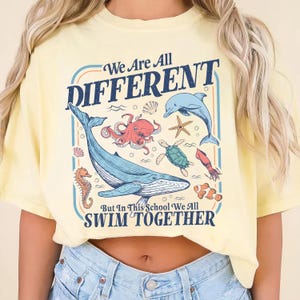 May include: Yellow t-shirt with a graphic featuring various sea creatures, including a whale, octopus, and dolphin, with the text "We Are All DIFFERENT But In This School We All SWIM TOGETHER."