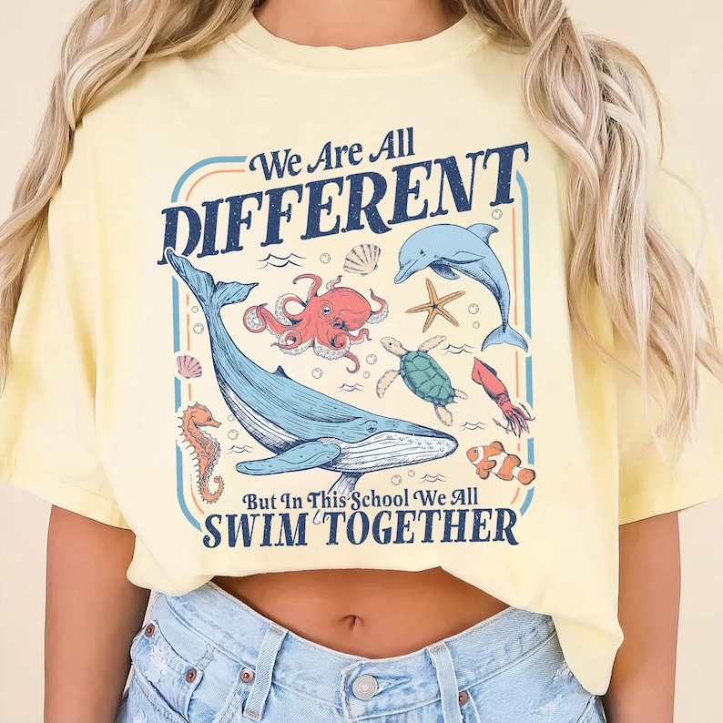 May include: Yellow t-shirt with a graphic featuring various sea creatures, including a whale, octopus, and dolphin, with the text "We Are All DIFFERENT But In This School We All SWIM TOGETHER."