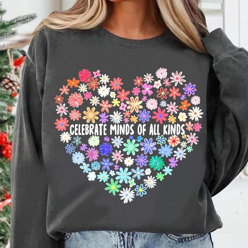 May include: A charcoal grey sweatshirt with a large heart-shaped design made of colorful flowers. The text "CELEBRATE MINDS OF ALL KINDS" is printed inside the heart.