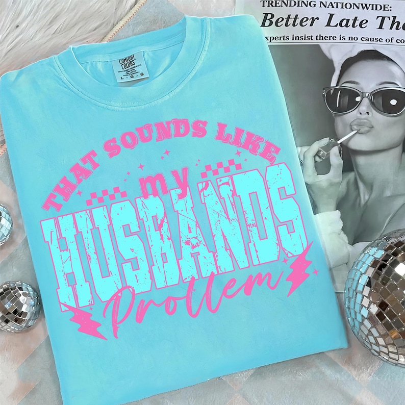 May include: A light blue Comfort Colors t-shirt with the text "THAT SOUNDS LIKE my HUSBANDS Problem" in pink and light blue. The shirt has a crew neck and short sleeves. A fun, casual tee.