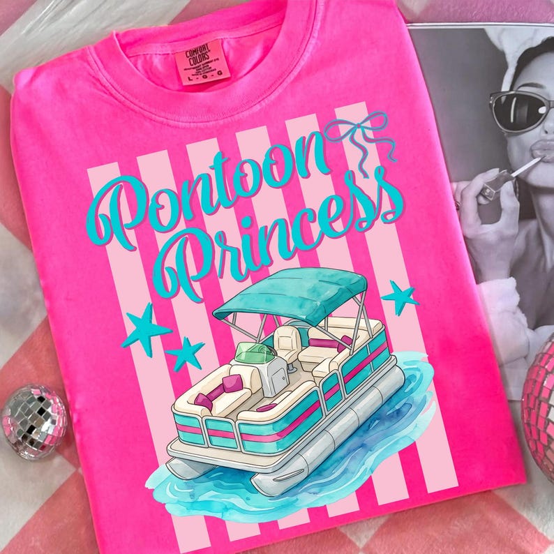 May include: A hot pink t-shirt with the words "Pontoon Princess" in turquoise script. The shirt features a graphic of a pontoon boat with a teal canopy and blue stars. The shirt is a Comfort Colors brand.
