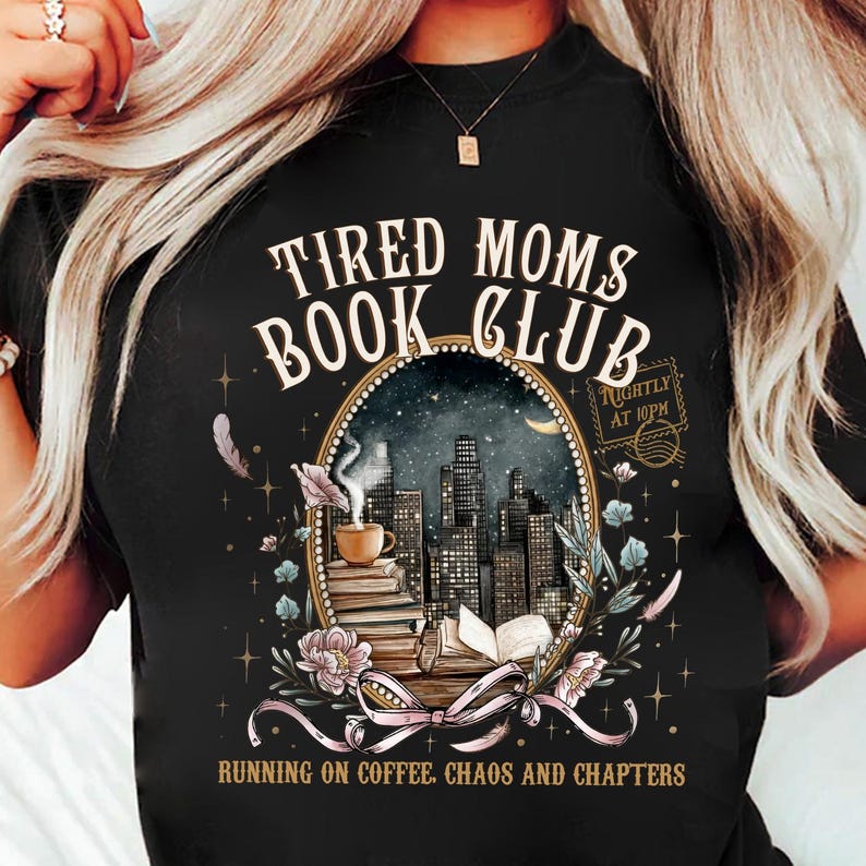 May include: Black t-shirt with the text "Tired Moms Book Club" in white script. The shirt features an oval design with a cityscape, books, coffee cup, and floral accents. The text "Running on Coffee, Chaos and Chapters" is also included.