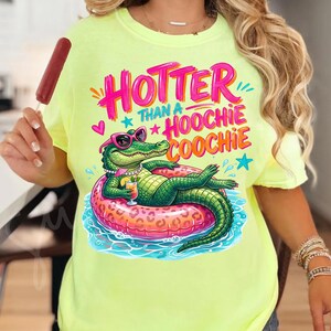 K&ouml;nnte beinhalten: Neongelbes T-Shirt mit einem Aufdruck eines Alligators mit Sonnenbrille, der auf einem rosa Schwimmring liegt. Der Text auf dem Shirt lautet "Hotter Than a Hoochie Coochie" in Pink und Orange.