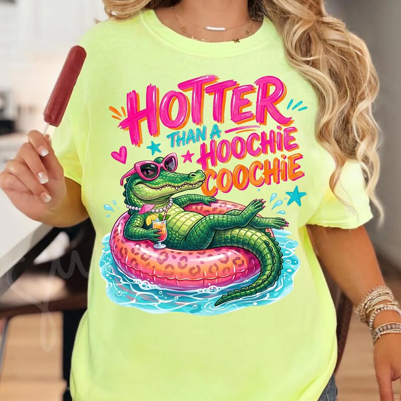 K&ouml;nnte beinhalten: Neongelbes T-Shirt mit einem Aufdruck eines Alligators mit Sonnenbrille, der auf einem rosa Schwimmring liegt. Der Text auf dem Shirt lautet "Hotter Than a Hoochie Coochie" in Pink und Orange.