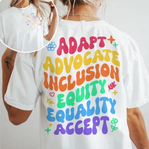 May include: White t-shirt with a rainbow-colored graphic on the back that says "ADAPT + ADVOCATE + INCLUSION + EQUITY + EQUALITY + ACCEPT".