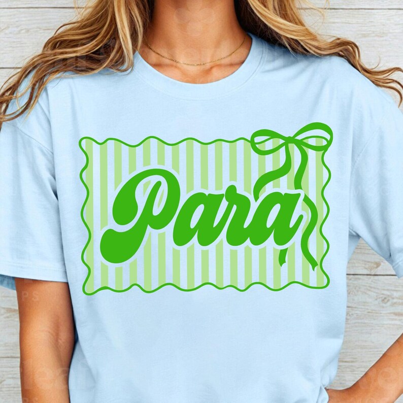 May include: Light blue t-shirt with a green graphic that says "Para" in a playful font. The graphic is framed by a green scalloped border and features a bow at the top right corner. The background of the graphic has vertical stripes.