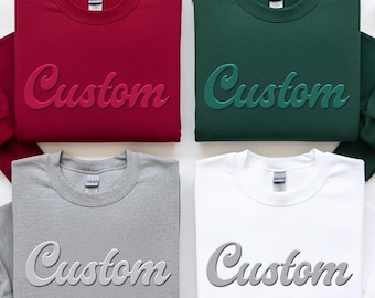 May include: Four crewneck sweatshirts in red, green, gray, and white. Each sweatshirt has the word "Custom" in a 3D script font across the front. The sweatshirts are displayed on a white surface.