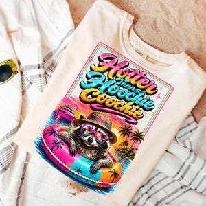 May include: Cream-colored sweatshirt featuring a graphic of a raccoon wearing sunglasses and a straw hat, floating in an inner tube. The graphic includes the text "Hotter Than a Hoochie Coochie" in colorful lettering, with a tropical beach scene background.