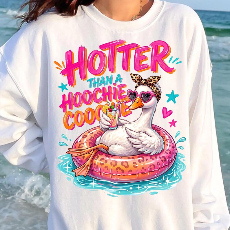 K&ouml;nnte beinhalten: Wei&szlig;es Sweatshirt mit einer Grafik einer Gans mit herzf&ouml;rmiger Sonnenbrille und Leoparden-Stirnband, die in einem rosa Schwimmring schwimmt. Der Text lautet "HOTTER THAN A HOOCHIE COOCHIE".