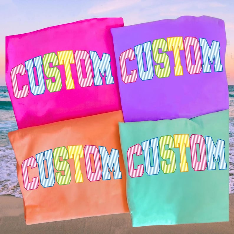 May include: Four colorful t-shirts in pink, purple, orange, and green, each with the word "CUSTOM" in a bold, multi-colored, collegiate-style font. The shirts are arranged on a beach background.