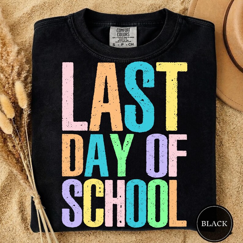 May include: Black t-shirt with the text "LAST DAY OF SCHOOL" in large, colorful, block letters. The letters are in pastel colors: pink, orange, blue, yellow, green, and purple. The shirt has a crew neck and short sleeves.