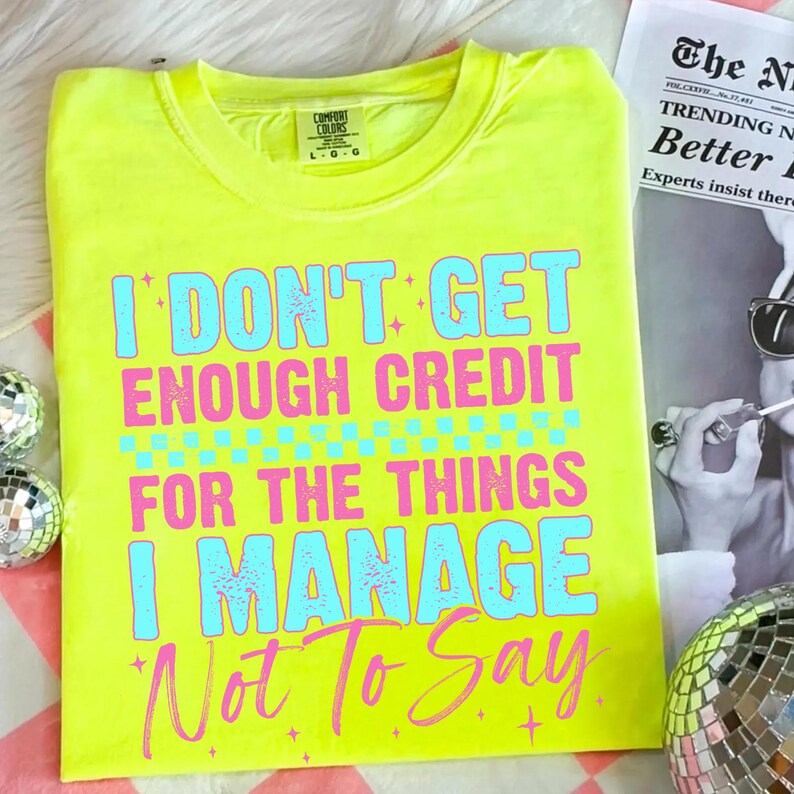 May include: Neon yellow t-shirt with the text "I DON'T GET ENOUGH CREDIT FOR THE THINGS I MANAGE Not To Say" in blue and pink. The shirt is a crew neck and has a tag that says "Comfort Colors".