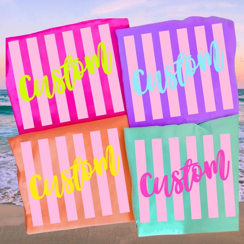 K&ouml;nnte beinhalten: Vier farbenfrohe Strandt&uuml;cher mit vertikalen rosa und wei&szlig;en Streifen. Jedes Handtuch tr&auml;gt das Wort "Custom" in einer anderen Farbe: Neongr&uuml;n, Hellblau, Gelb und Pink. Die Handt&uuml;cher sind an einem Strand angeordnet.